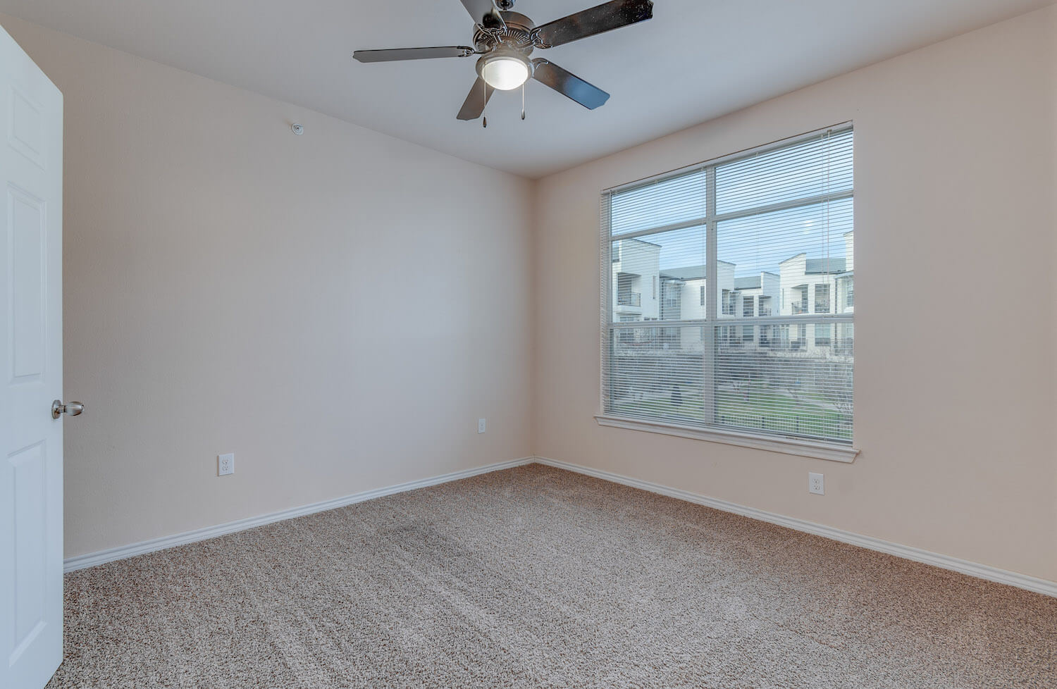 Another look at the large bedroom with carpet, a ceiling fan, and a window.