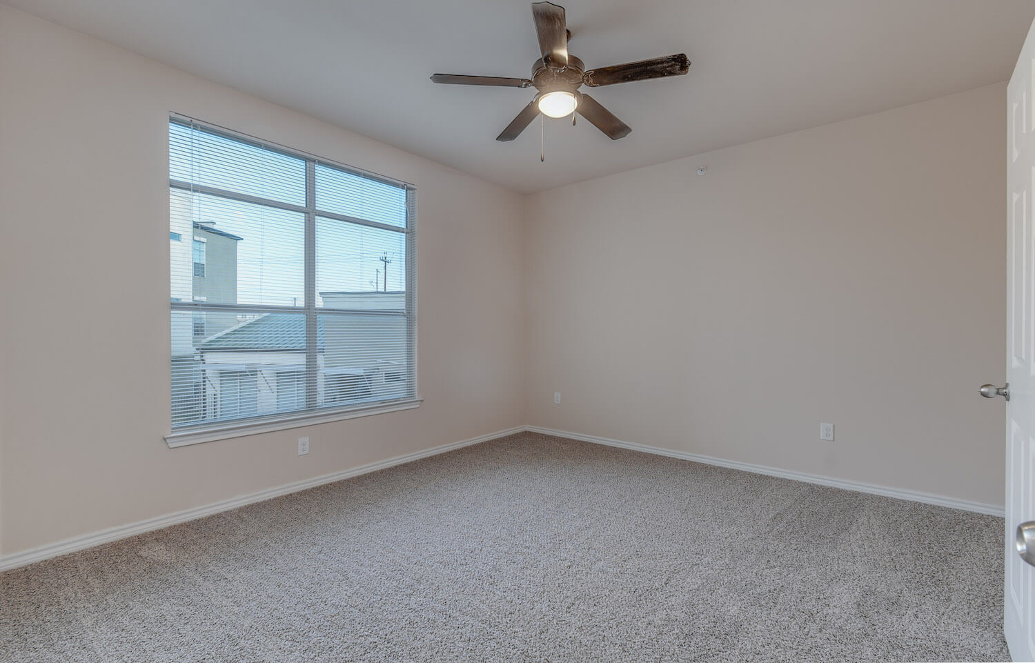 The carpeted bedroom with a ceiling fan and large window.