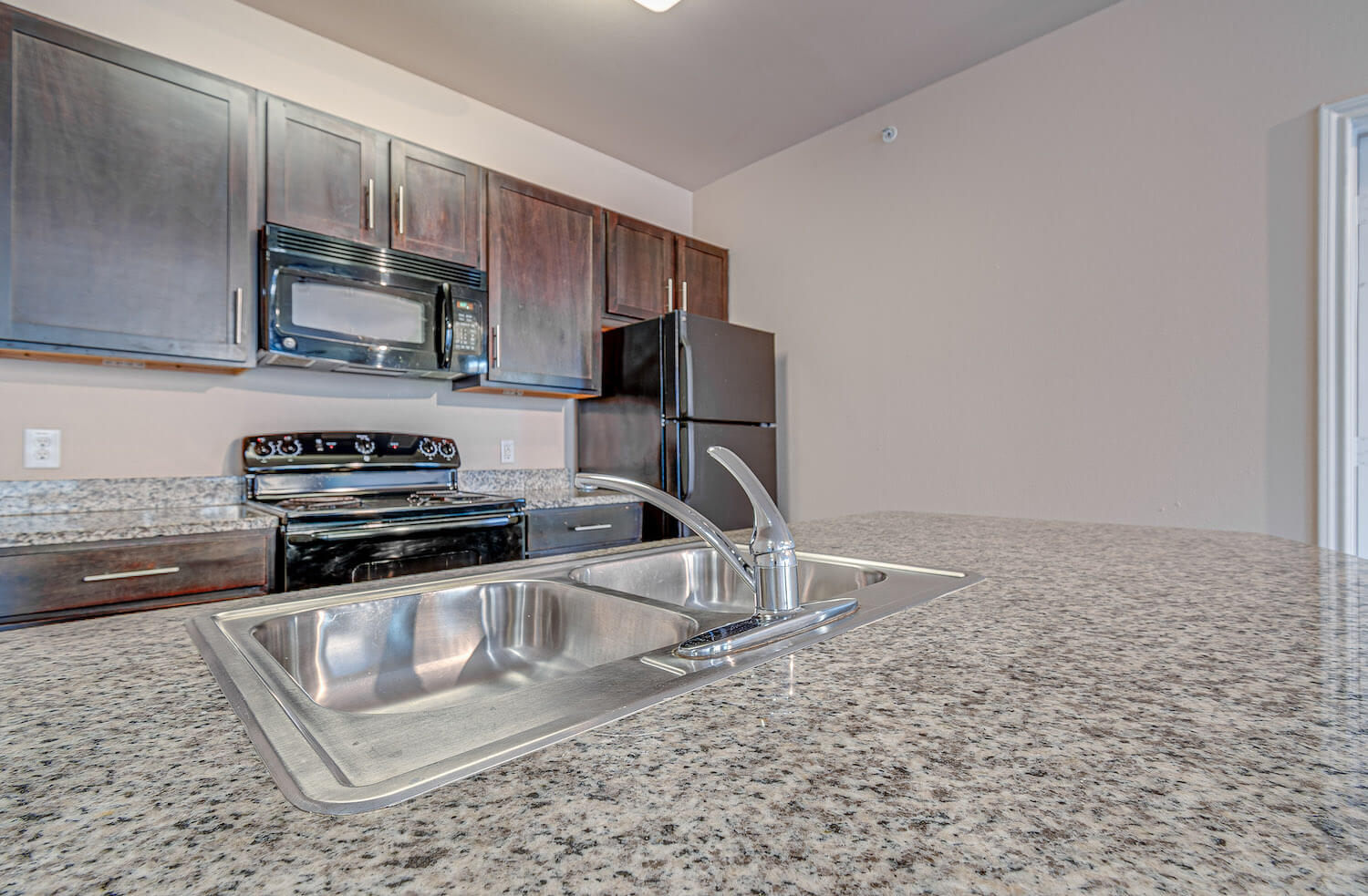 A large granite counter top reflecting the black appliances.